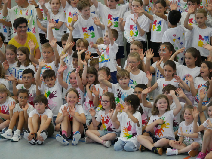 lachende Kinder sitzen winkend auf dem Boden